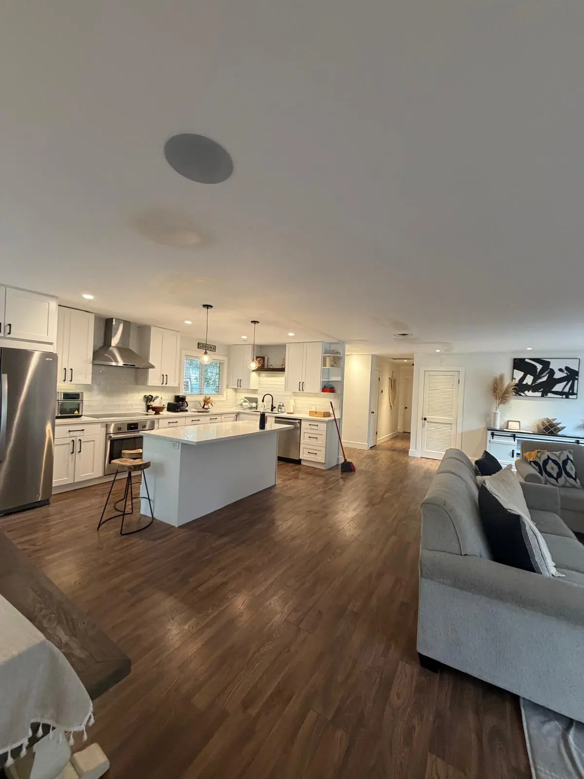 Finished open-plan kitchen and living room, with white cabinets, a quartz island, and new wood-look flooring